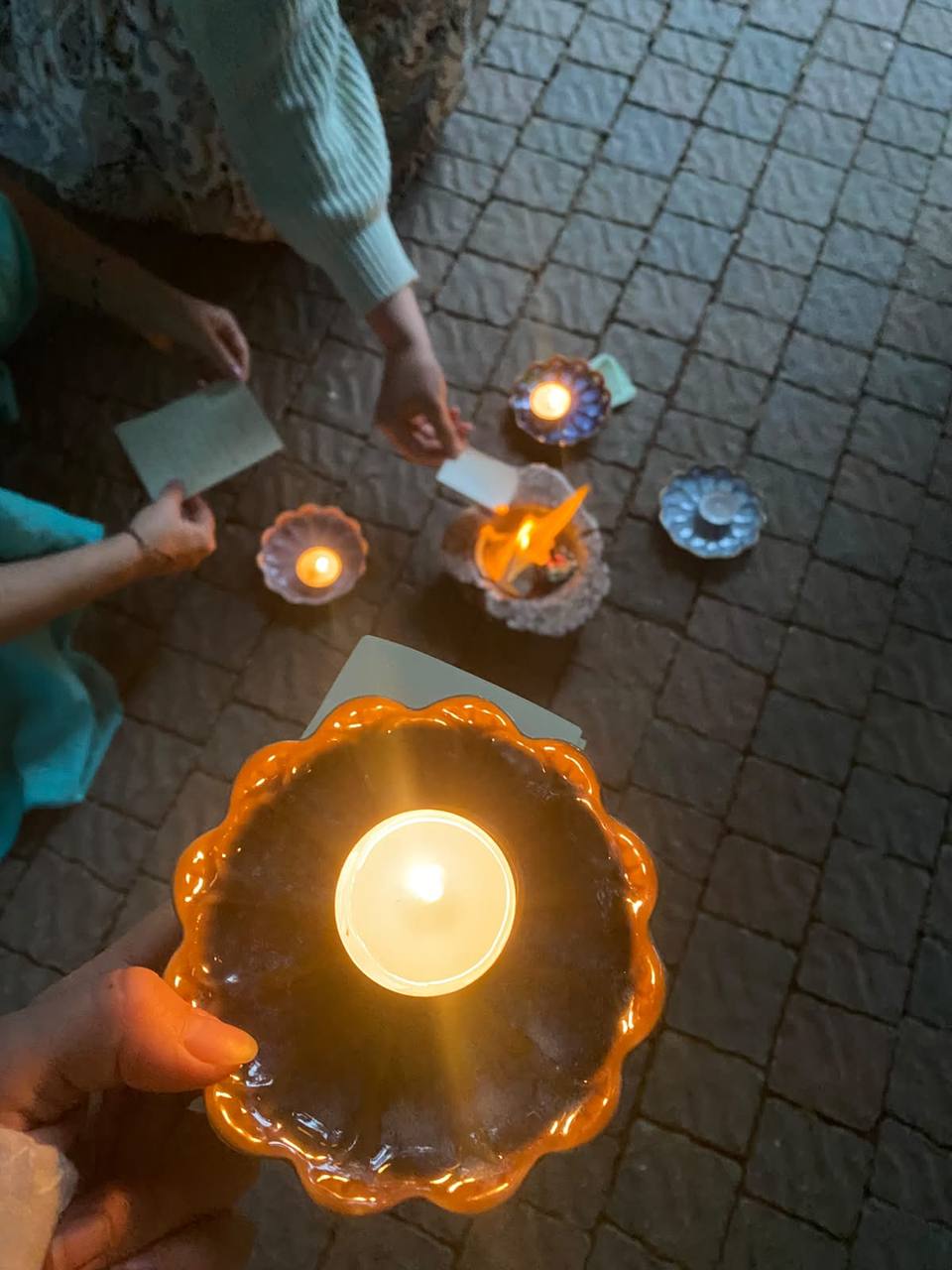 Hände halten Teelichter über beschriebenen Zetteln bei einem Abendritual
